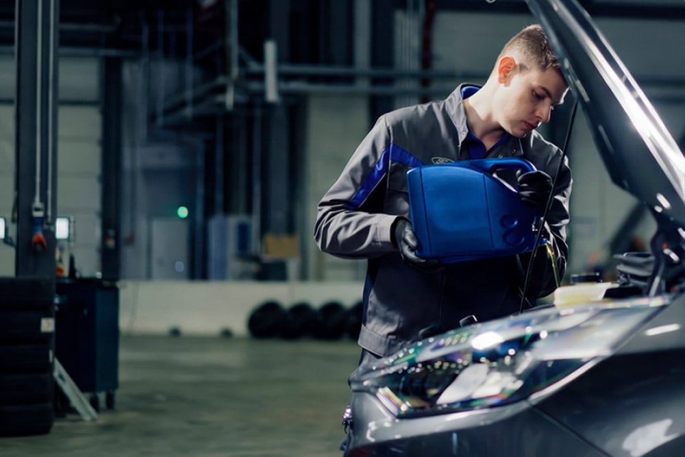 Widok z boku na autoryzowanego technika Ford naprawiającego pojazd w warsztacie.