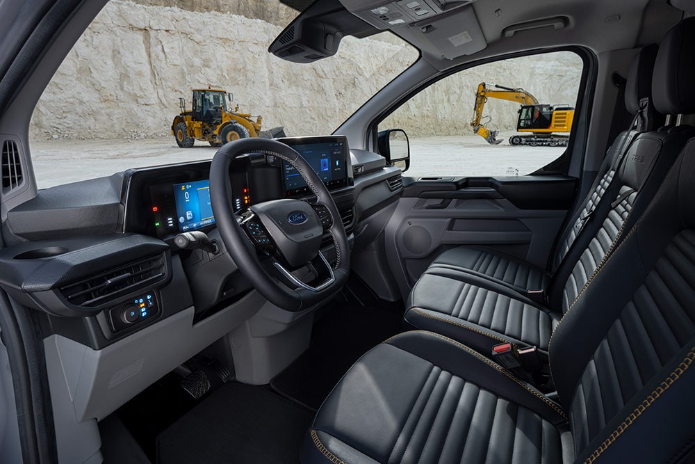 Widok wnętrza furgonetki Ford Transit Custom przedstawiający deskę rozdzielczą, kierownicę i siedzenia.