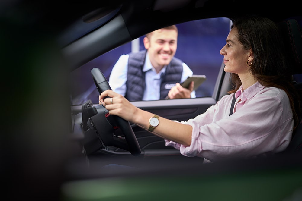 Osoba siedząca w fotelu kierowcy samochodu Ford patrzy na technika stojącego na zewnątrz auta z tabletem w ręce.
