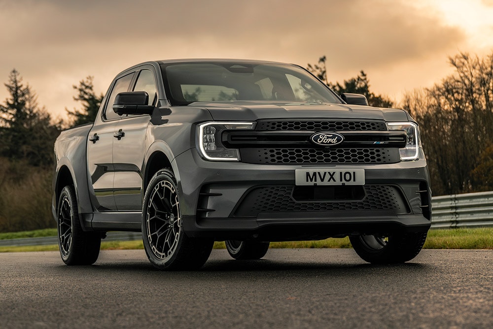Szary Ford Pro Ranger Plug-in Hybrid zaparkowany na mokrej drodze, w tle drzewa.
