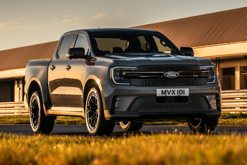  Srebrny Ford Pro Ranger Plug-in Hybrid zaparkowany przed budynkiem przemysłowym.