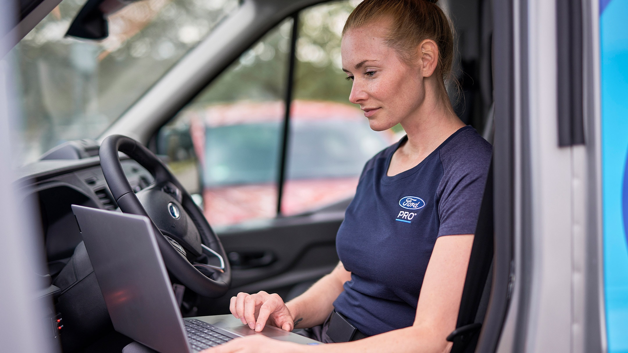 Ekspert Ford Pro siedzi w samochodzie i sprawdza laptopa podczas serwisu pojazdu Ford.